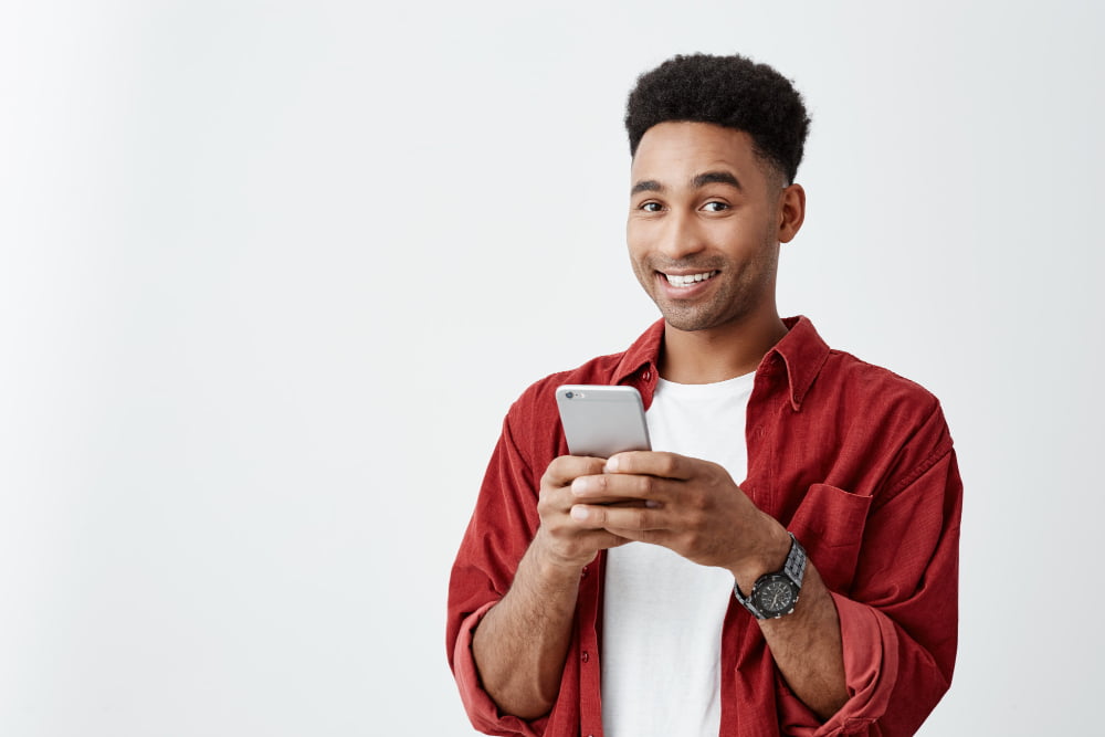 Detran RS disponibiliza apresentação de condutor infrator também pela Carteira Digital de Trânsito 4 positive emotions close up young good looking dark skinned male with afro hairstyle white t shirt red shirt smiling with teeth chatting with friend smartphone